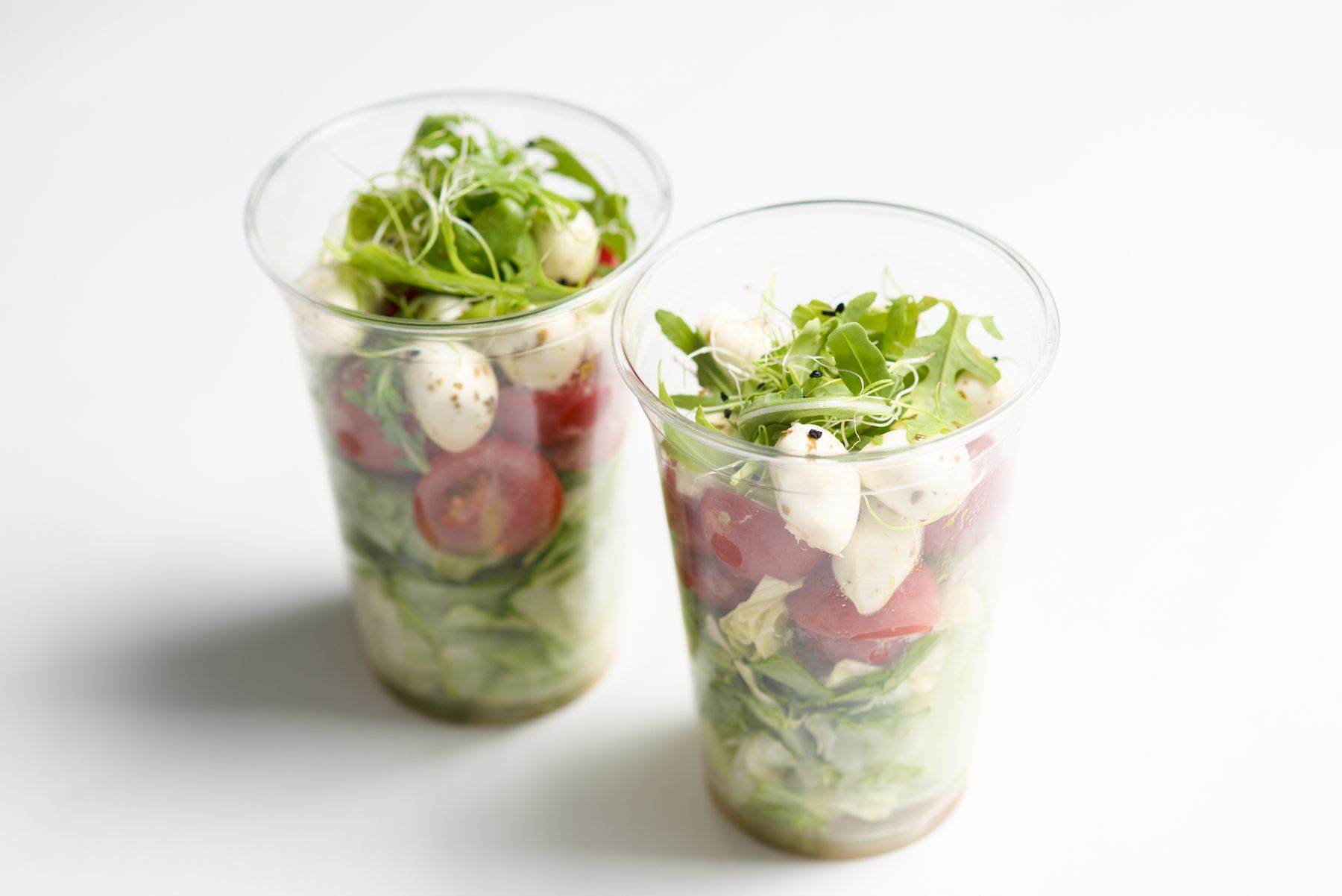 Due bicchieri trasparenti con insalata, rucola, pomodorini e mozzarella