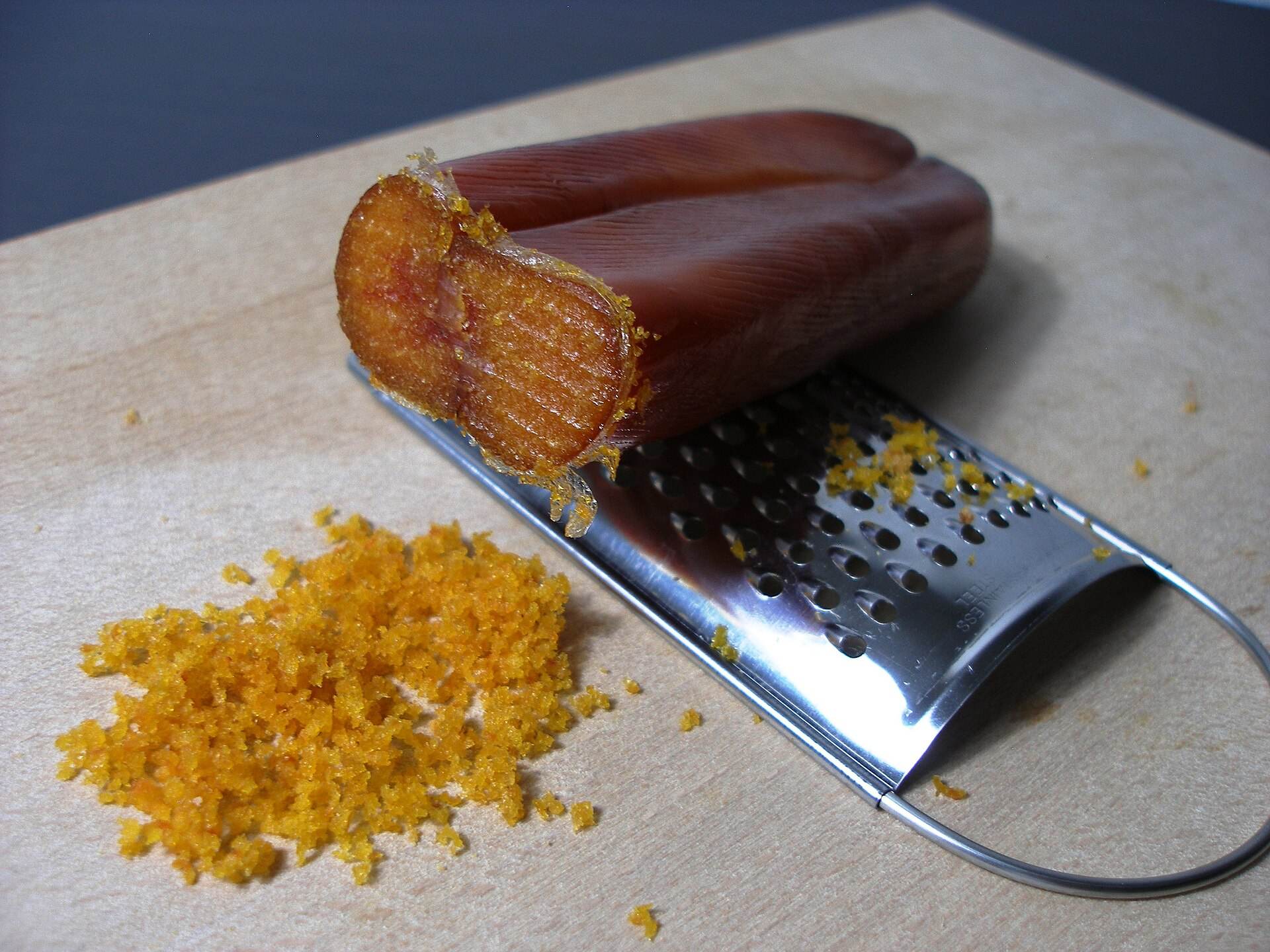 Una bottarga intera con la grattugia e la polvere gialla grattugiata