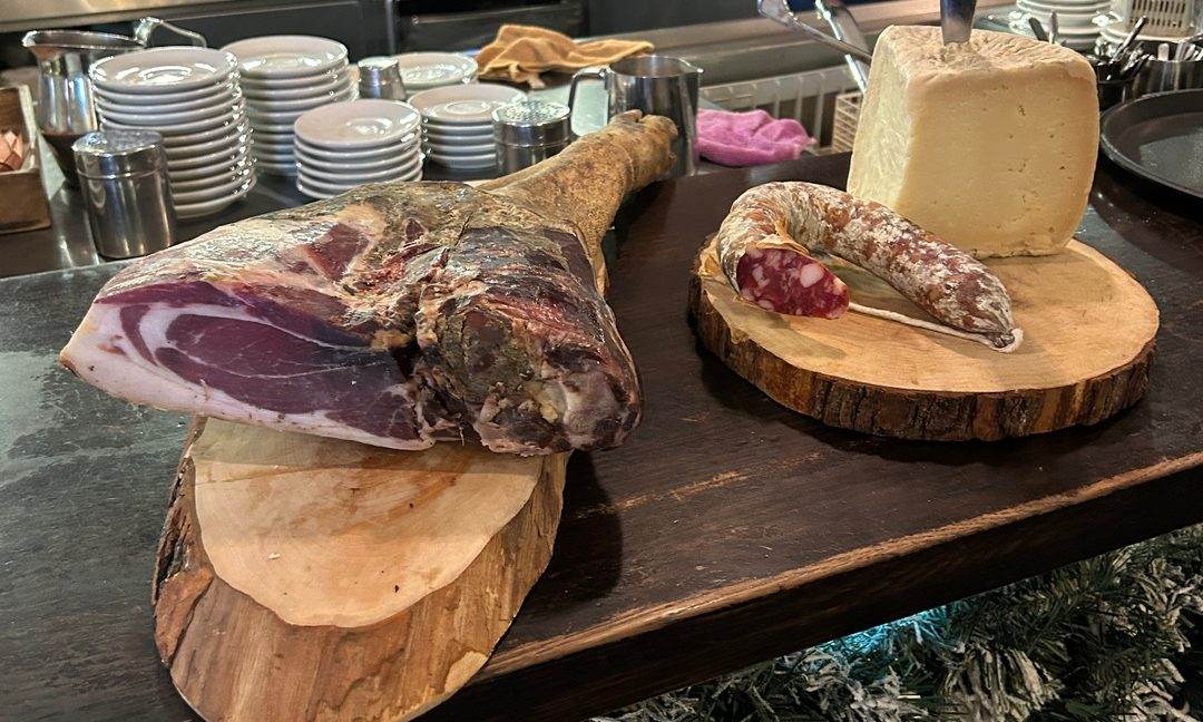 Un prosciutto e un salame su tagliere di legno, con il pecorino